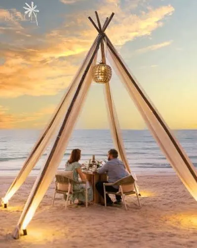 Couple dining under a lantern-lit tent on the beach at sunset