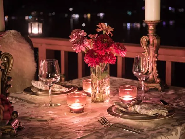 Candlelit table for two with red flowers on a terrace at night