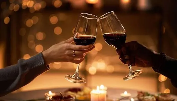 Two glasses of red wine clinking in candlelight